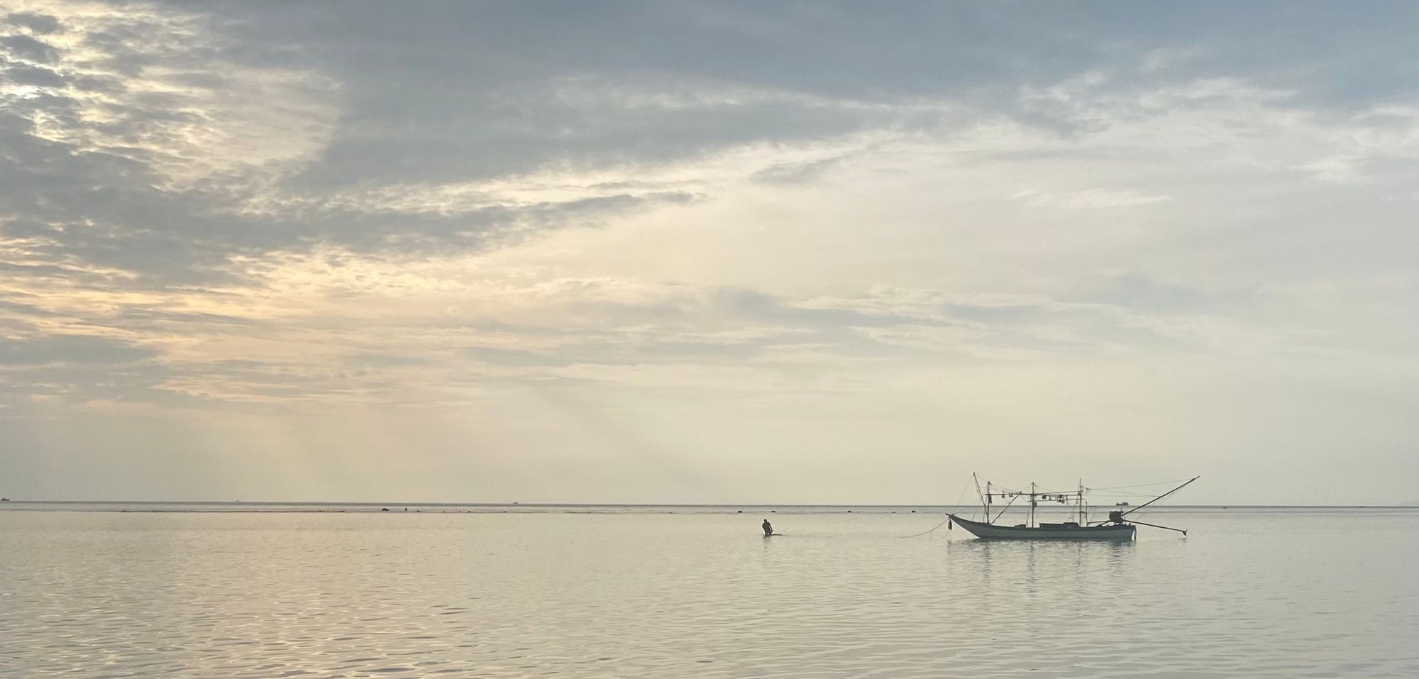 Dawn over a calm sea, a small fishing boat lying at anchor